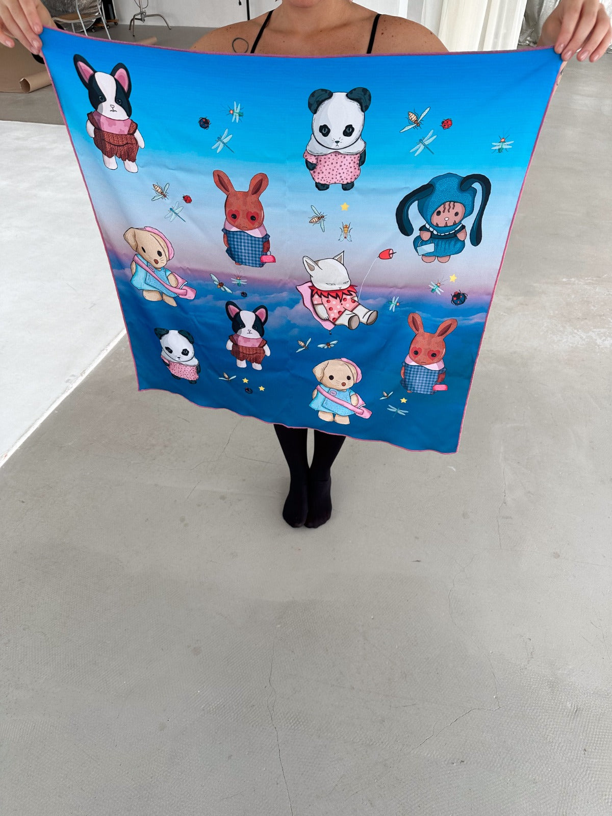 Close-up of a person showcasing a silk scarf with illustrated animal characters such as dogs and pandas, set against a serene, sky-like backdrop. The scarf’s playful design makes it perfect for adding personality to any wardrobe. Best for those looking for whimsical fashion pieces.
