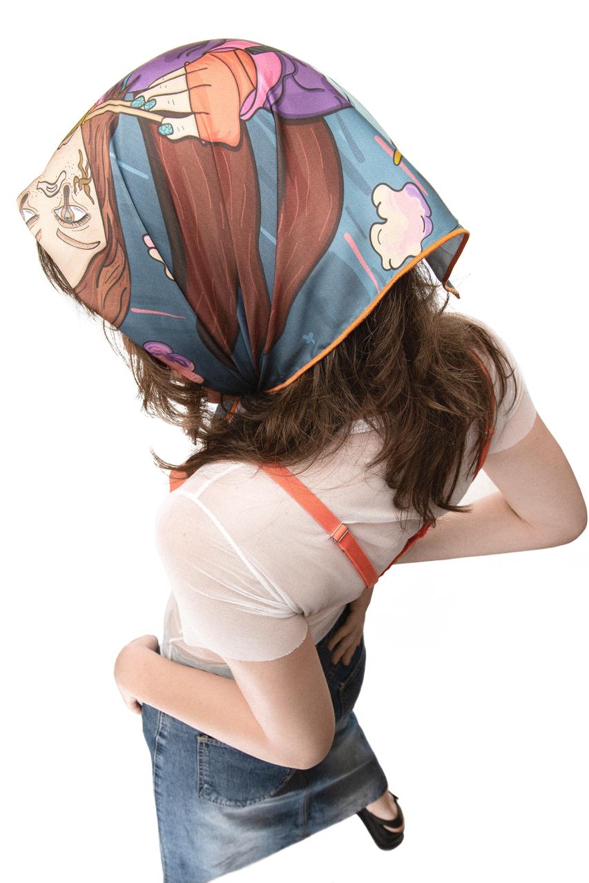 A photo of a person wearing a colorful square scarf on their head with a cartoon-like design featuring a woman eating ramen, standing with their back to the camera and their head tilted downwards, against a white background.