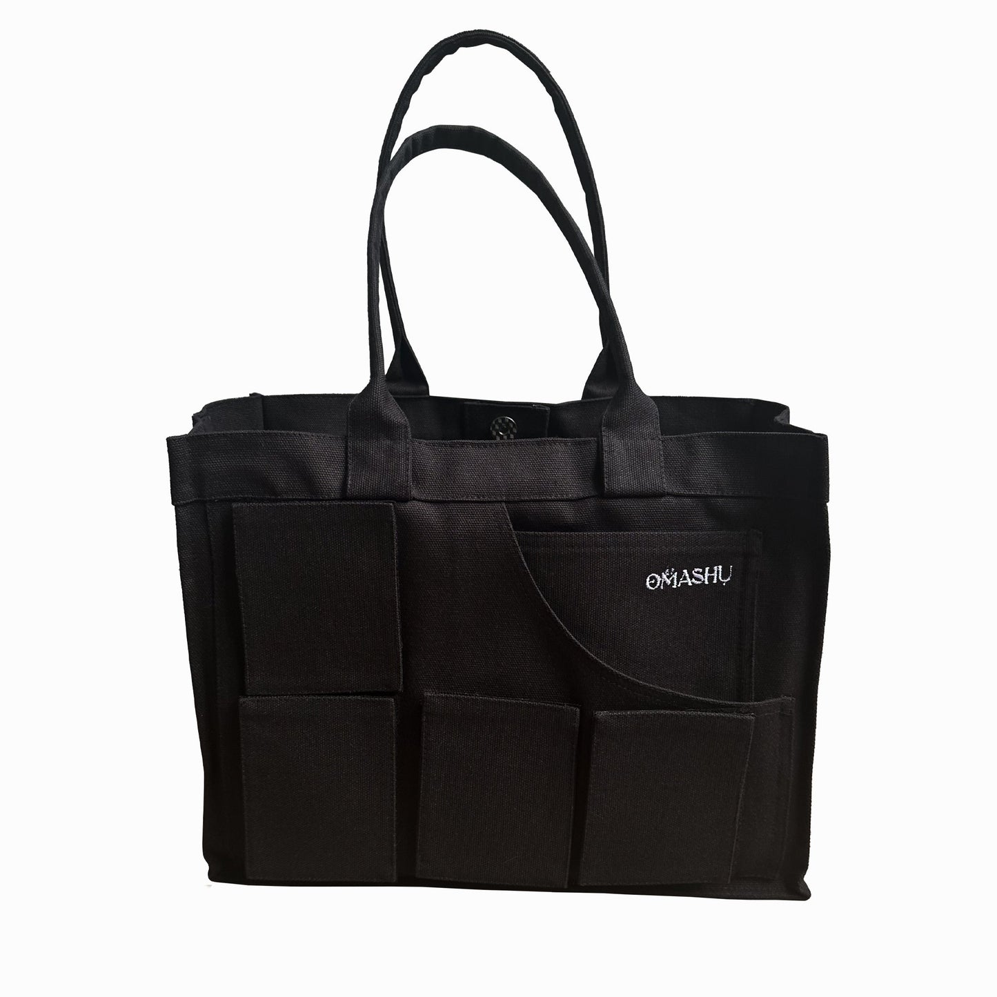 A black tote bag with multiple exterior pockets, featuring a simple design and sturdy handles. The brand name 'Omashu' is embroidered in white on one of the pockets.