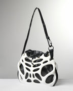 A white and black sculptural shoulder bag with an organic, open-frame structure and a black strap, photographed on a light gray studio background.