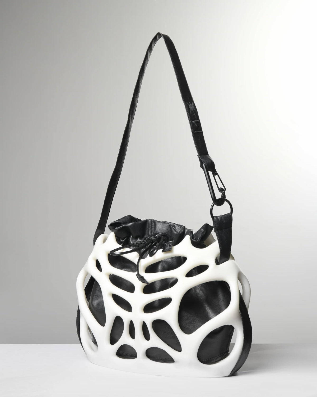 A white and black sculptural shoulder bag with an organic, open-frame structure and a black strap, photographed on a light gray studio background.