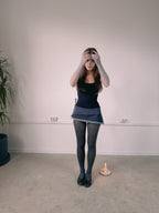 Person wearing a black top and denim skirt standing in a room with a white wall and a candle on the floor.