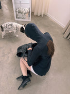 Person sitting on the floor with a dog looking at them in a room.
