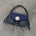 Blue handbag with black fringes on a concrete floor