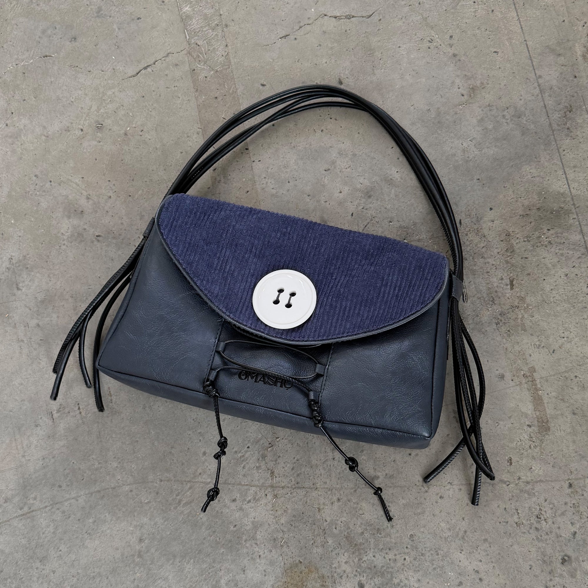Blue handbag with black fringes on a concrete floor