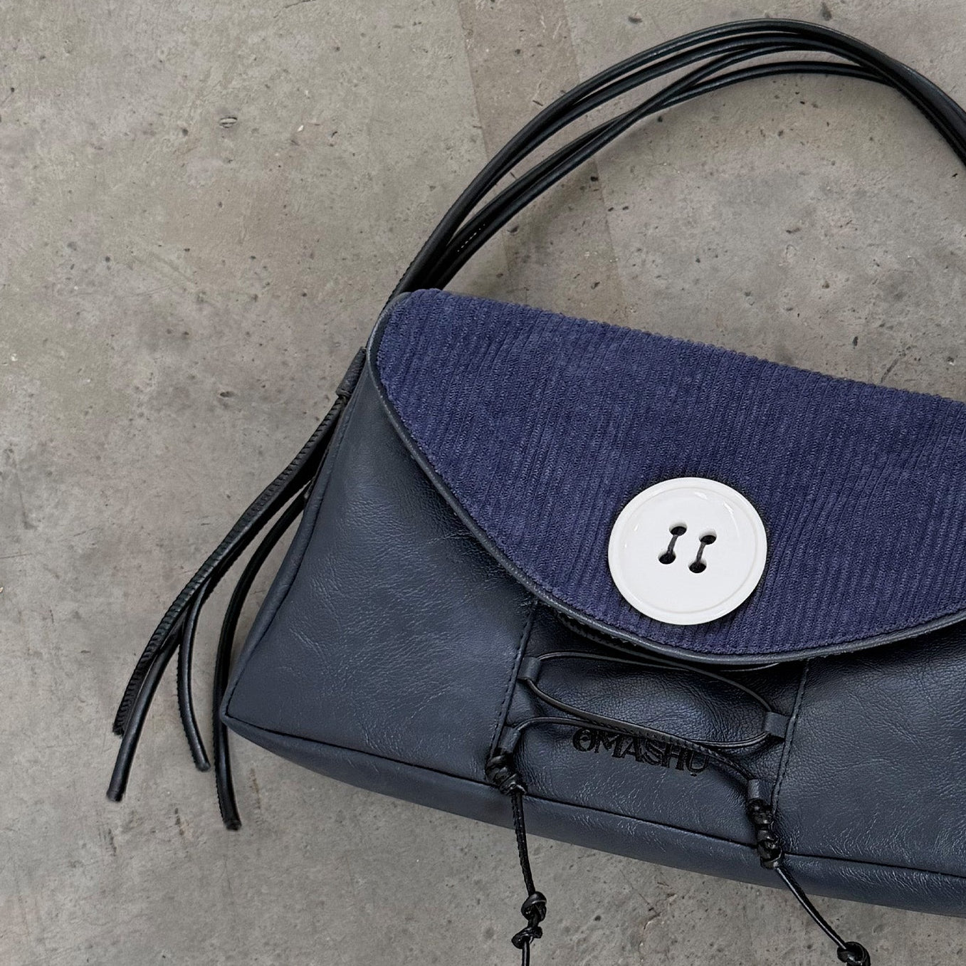 Blue handbag with black fringes on a concrete floor