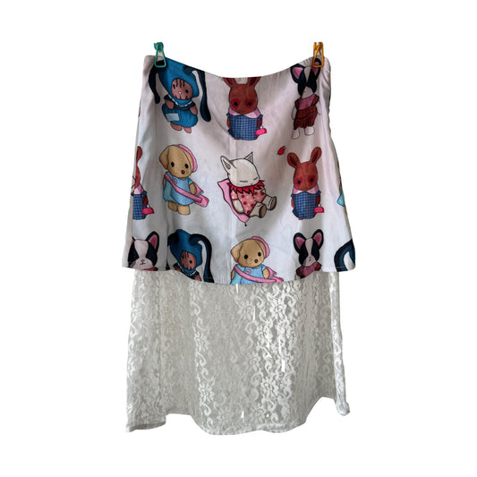 A white skirt adorned with colorful cartoon animals, including bunnies, dogs, and other characters. The upper section features the illustrations, while the lower part is made of sheer white lace fabric. The skirt is hung on a clothesline with two clips.