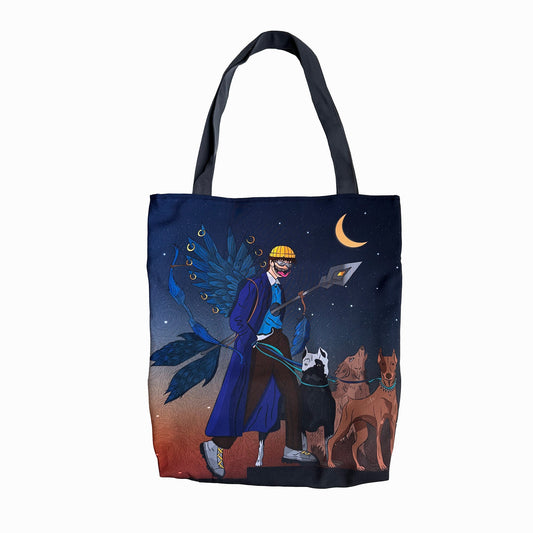 A photo of a Omashu tote bag with an illustration of a man in a blue coat and hat with a peacock feather in it, holding a lantern and accompanied by two dogs, against a dark blue sky background with a crescent moon and stars, with black handles and predominantly blue, orange, and brown colors in the illustration.