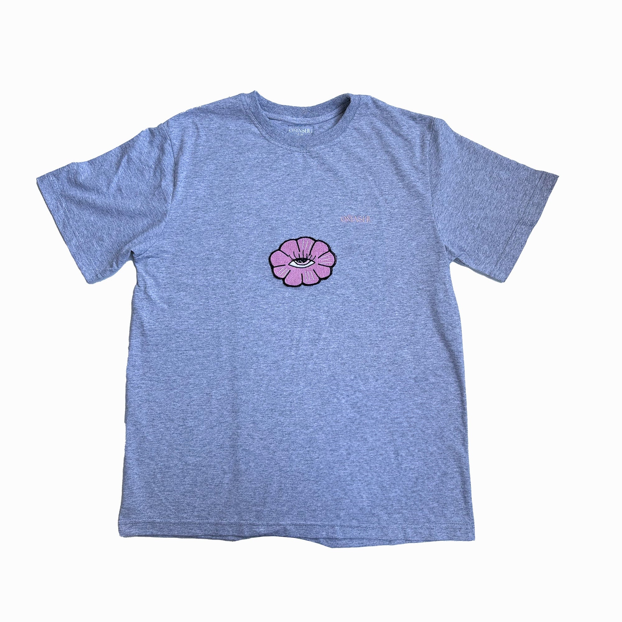 a t-shirt with flower design. The flower design is a simple line drawing of a pink flower with five petals and eye inside. The word “Omashu” is written in cursive above the flower design. The t-shirt is gray ,short-sleeved and has a crew neck.