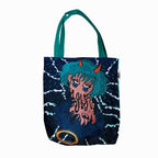 A tote bag with a graphic design on it. The tote bag is dark blue in color with a teal handle. The graphic design is of a girl with horns and a fish tail. She is holding up a peace sign with her fingers. The girl is surrounded by dark blue waves. The design is in a cartoon style. The bottom right corner of the tote bag has a goldfish in a bubble.